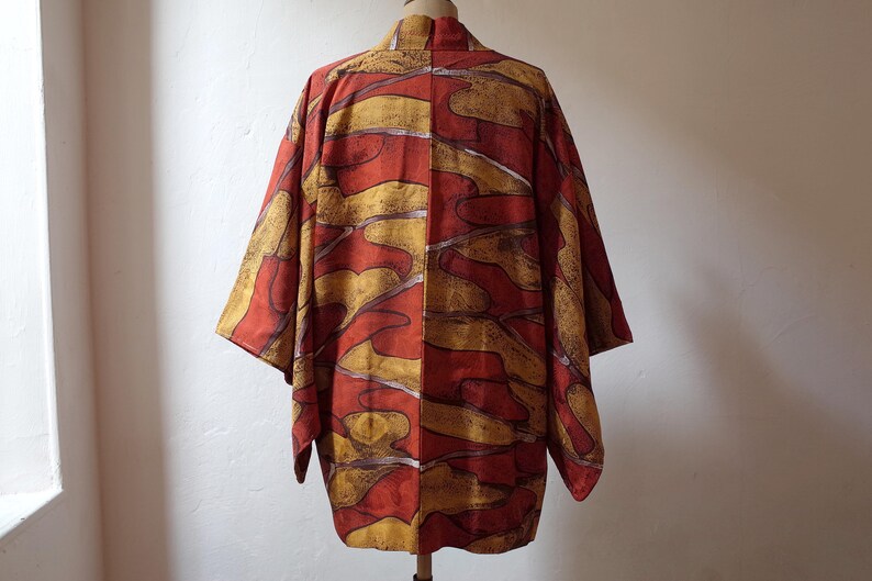 May include: A red and gold Japanese kimono with an abstract pattern. The kimono is made of a soft, flowing fabric and has a relaxed fit.