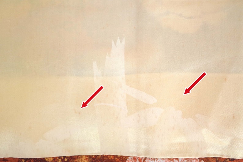 May include: A close-up of a light beige fabric with two white stains. The stains are highlighted with red arrows.