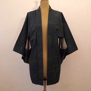 May include: A dark blue Japanese kimono with a subtle pattern of white and green leaves. The kimono is open in the front and has long sleeves.