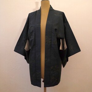 Op de afbeelding: Een donkerblauwe kimono met een subtiel patroon van groene bladeren. De kimono is open aan de voorkant en heeft lange mouwen.