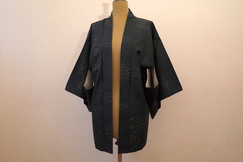 Op de afbeelding: Een donkerblauwe kimono met een subtiel patroon van groene bladeren. De kimono is open aan de voorkant en heeft lange mouwen.