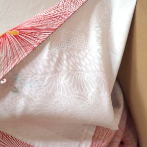 May include: A white kimono with a red and yellow floral pattern. The kimono is folded in half and the inside of the fabric is visible.