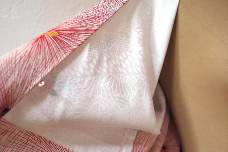 May include: A white kimono with a red and yellow floral pattern. The kimono is folded in half and the inside of the fabric is visible.