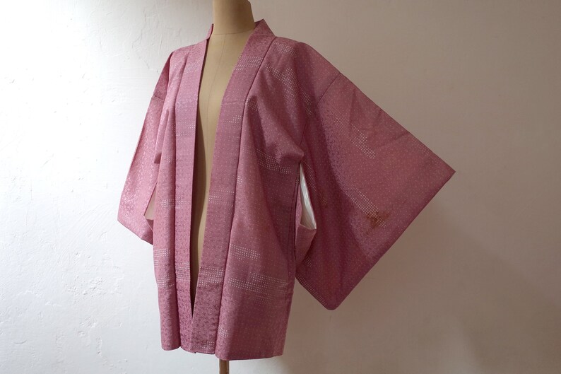 Puede incluir: Un kimono japon&eacute;s de color rosa y blanco con un forro blanco. El kimono est&aacute; abierto por delante y tiene mangas largas.