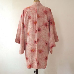 May include: A pink and white kimono with a floral pattern. The kimono has a long, flowing silhouette and is made of a lightweight fabric.