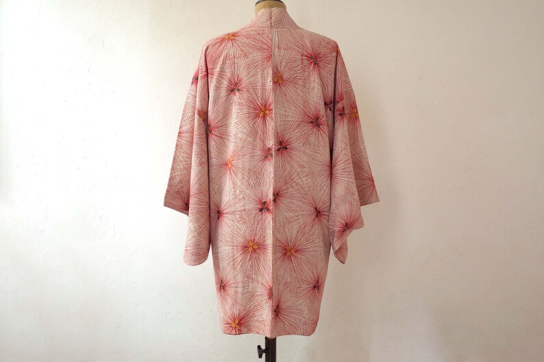 May include: A pink and white kimono with a floral pattern. The kimono has a long, flowing silhouette and is made of a lightweight fabric.