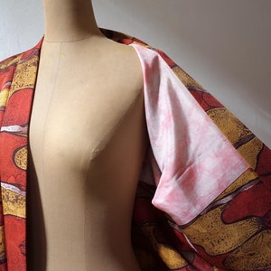 May include: A red and gold patterned kimono with a pink lining. The kimono is open in the front, revealing the lining.