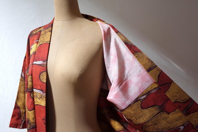May include: A red and gold patterned kimono with a pink lining. The kimono is open in the front, revealing the lining.