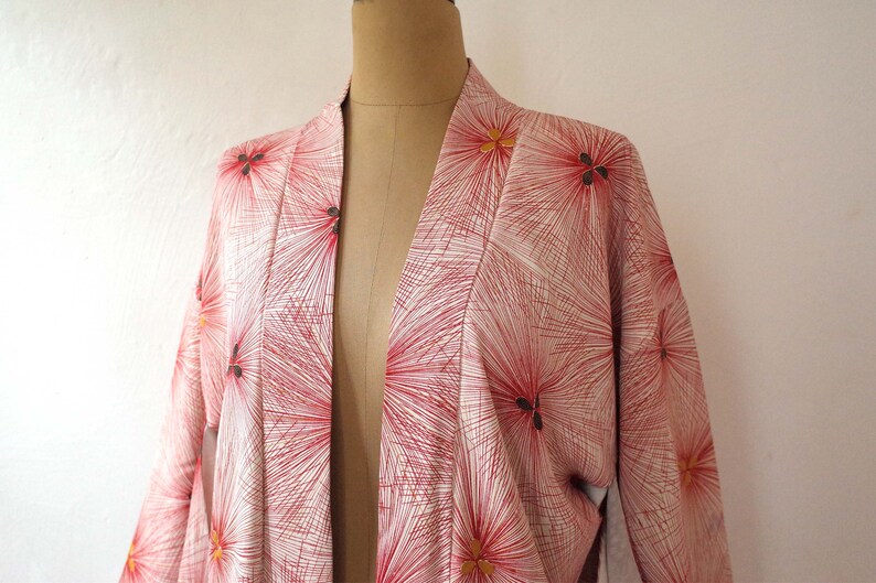 May include: A white kimono with a red and gold floral pattern. The kimono is open in the front and has long sleeves.