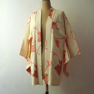Puede incluir: Un kimono de color crema con un estampado floral en tonos naranja. El kimono est&aacute; hecho de una tela suave y sedosa y tiene un corte holgado.