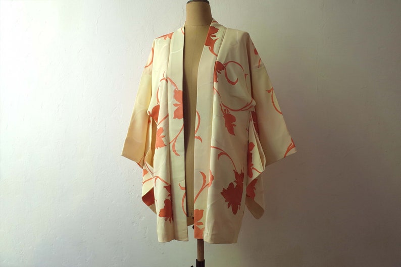 Puede incluir: Un kimono de color crema con un estampado floral en tonos naranja. El kimono est&aacute; hecho de una tela suave y sedosa y tiene un corte holgado.