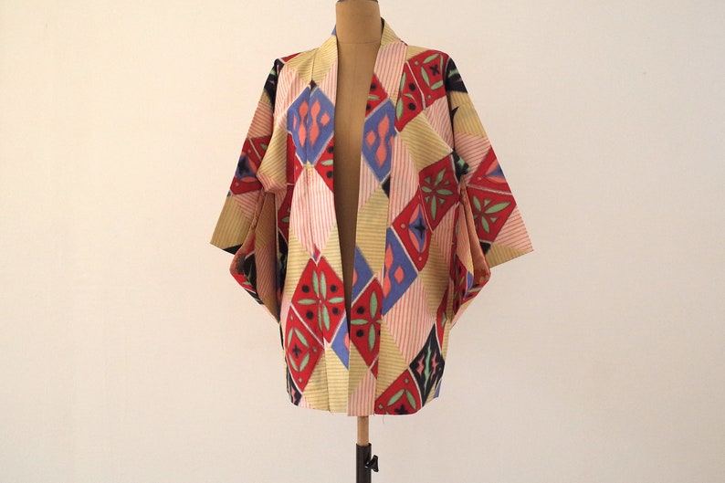 May include: A colorful kimono with a geometric pattern in shades of red, blue, yellow, and black. The kimono is made of a lightweight fabric and has a relaxed fit.