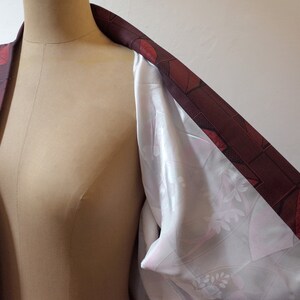 May include: A burgundy kimono with a geometric pattern of red leaves and squares. The kimono is lined with a white fabric with a floral pattern.