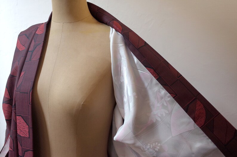 May include: A burgundy kimono with a geometric pattern of red leaves and squares. The kimono is lined with a white fabric with a floral pattern.