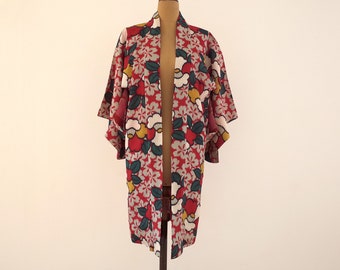 Könnte beinhalten: Ein roter Kimono mit einem floralen Muster in Weiß-, Gelb- und Grüntönen. Der Kimono hat einen weiten, offenen Kragen und lange Ärmel.