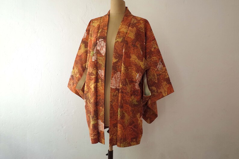 May include: A brown and orange kimono with a leaf pattern. The kimono is open in the front and has a long, flowing silhouette.