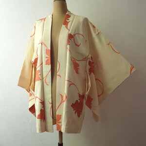 Puede incluir: Un kimono de color crema con un patr&oacute;n floral en tonos naranja. El kimono tiene un cuello ancho y abierto y mangas largas.