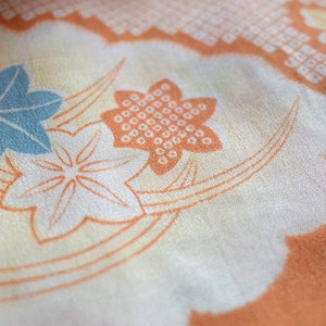 May include: A close-up of a fabric with a floral pattern. The fabric is a light orange color with white and blue flowers. The flowers are stylized and have a geometric design.