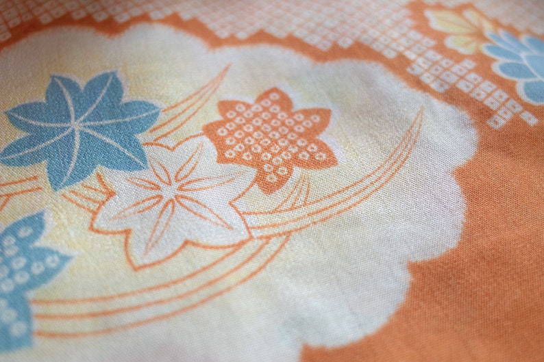May include: A close-up of a fabric with a floral pattern. The fabric is a light orange color with white and blue flowers. The flowers are stylized and have a geometric design.