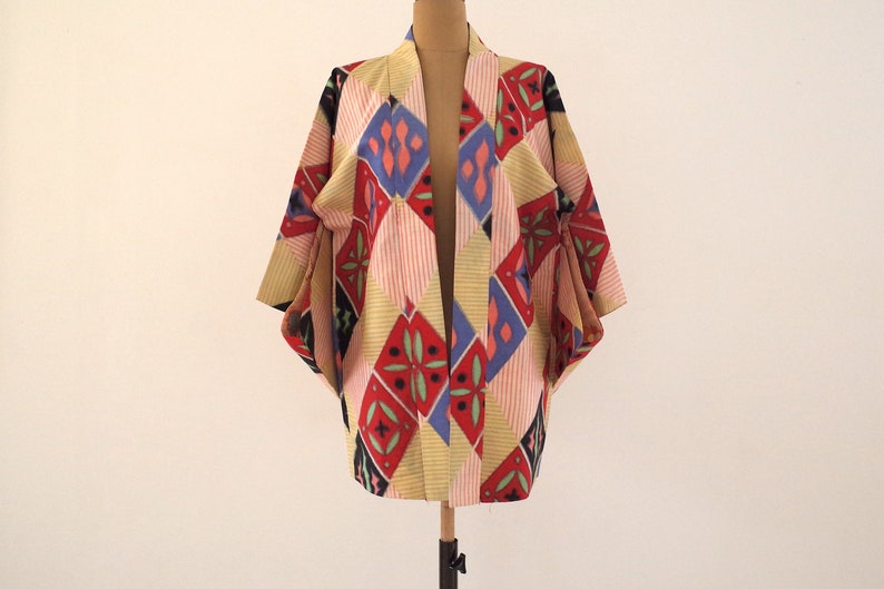 May include: A colorful kimono with a geometric pattern in shades of red, blue, yellow, and green. The kimono is made of a lightweight fabric and has a relaxed fit.