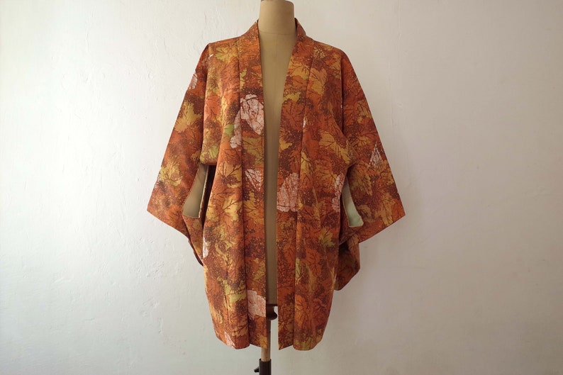 May include: A brown and orange kimono with a leaf pattern. The kimono is open in the front and has long sleeves.