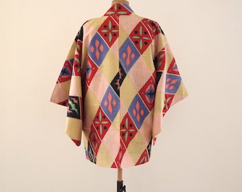 Puede incluir: Una chaqueta haori japonesa tradicional con un patrón geométrico colorido en tonos de rojo, azul, amarillo y negro. El haori está hecho de una tela ligera y tiene un corte holgado.