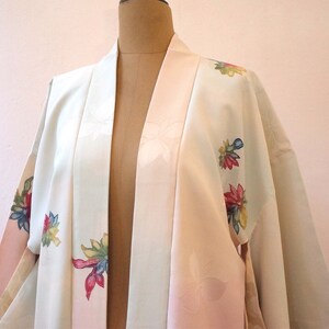 K&ouml;nnte beinhalten: Ein wei&szlig;er und rosa japanischer Kimono mit Blumenstickerei. Der Kimono hat einen rosa G&uuml;rtel und ist mit bunten Blumen verziert.
