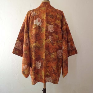 May include: A brown and gold kimono with a floral pattern. The kimono has a traditional Japanese design with a wide collar and long sleeves.