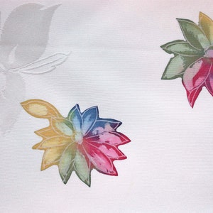 K&ouml;nnte beinhalten: Wei&szlig;er Stoff mit einem bunten Blumenmuster. Die Blumen sind mehrfarbig mit Schattierungen von Rot, Rosa, Gelb, Gr&uuml;n und Blau.