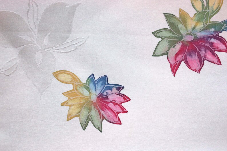 K&ouml;nnte beinhalten: Wei&szlig;er Stoff mit einem bunten Blumenmuster. Die Blumen sind mehrfarbig mit Schattierungen von Rot, Rosa, Gelb, Gr&uuml;n und Blau.