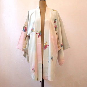 K&ouml;nnte beinhalten: Ein hellblauer und rosa japanischer Kimono mit Blumenmuster. Der Kimono hat einen weiten, offenen Kragen und lange &Auml;rmel. Der Stoff ist weich und seidig.