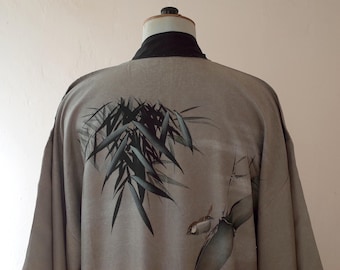 Puede incluir: Un kimono gris con cuello negro y diseño de bambú. El bambú está representado en tonos verdes y negros, creando una estética serena y natural. El kimono se exhibe en un maniquí.