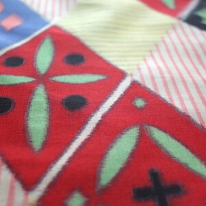 May include: A red fabric with a geometric pattern of green leaves and black circles. The fabric has a white and pink striped background.