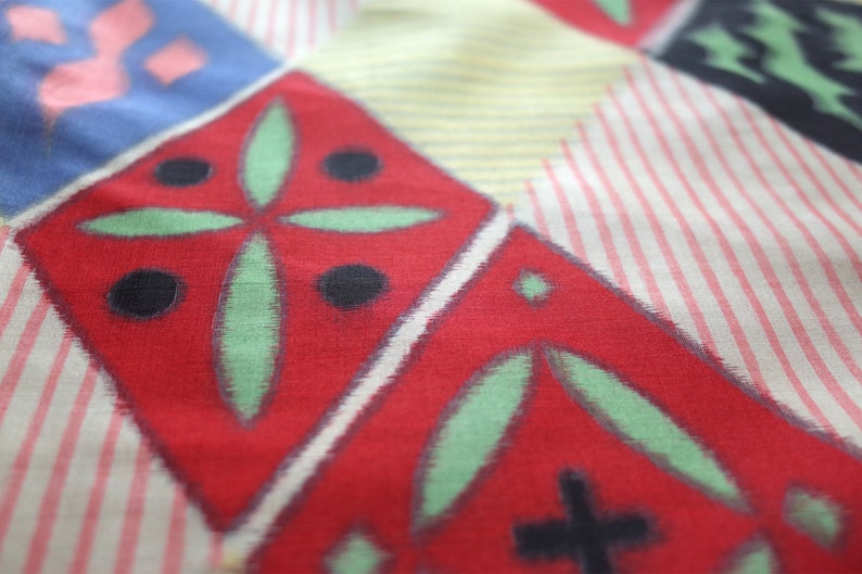 May include: A red fabric with a geometric pattern of green leaves and black circles. The fabric has a white and pink striped background.