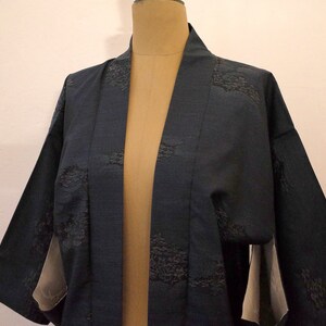 Op de afbeelding: Een donkerblauwe kimono met een subtiel patroon van zwarte geborduurde ontwerpen. De kimono is open aan de voorkant en heeft lange mouwen.