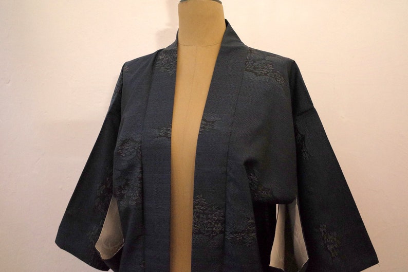 Op de afbeelding: Een donkerblauwe kimono met een subtiel patroon van zwarte geborduurde ontwerpen. De kimono is open aan de voorkant en heeft lange mouwen.