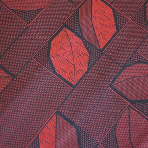 May include: Red fabric with a geometric pattern of black lines and red leaves. The fabric has a textured surface.