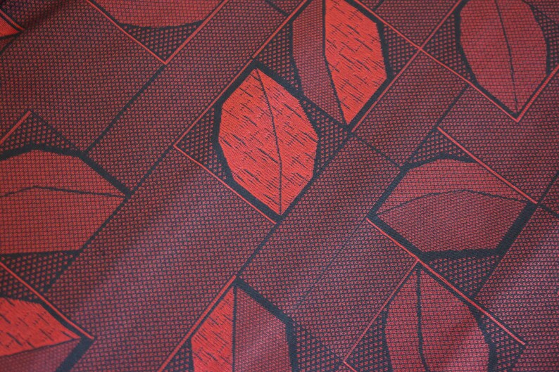 May include: Red fabric with a geometric pattern of black lines and red leaves. The fabric has a textured surface.
