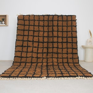 May include: A large, rectangular rug with a brown and black checkered pattern. The rug has a shaggy texture and a cream-colored fringe along the bottom edge. The rug is displayed on a light-colored floor.