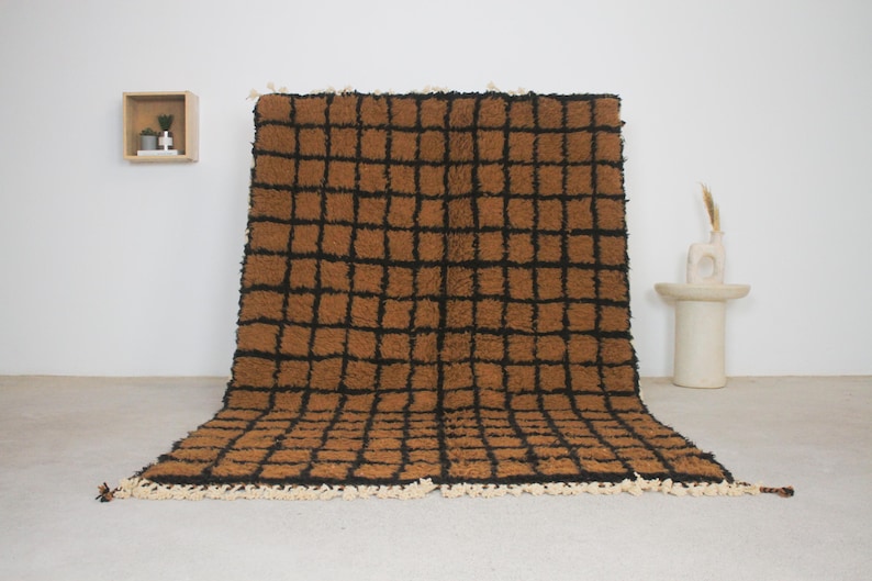 May include: A large, rectangular rug with a brown and black checkered pattern. The rug has a shaggy texture and a cream-colored fringe along the bottom edge. The rug is displayed on a light-colored floor.