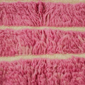 May include: Close-up of a pink and white striped rug with a fuzzy texture. The rug is made of woven fibers and has a soft, plush feel.