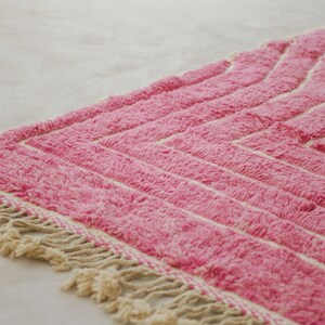 May include: Pink and white striped rug with a fringe border. The rug has a geometric pattern.