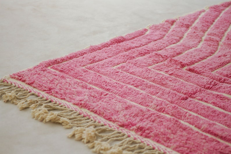 May include: Pink and white striped rug with a fringe border. The rug has a geometric pattern.