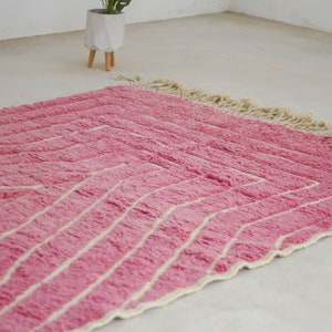 May include: A pink and white striped rug with a fringe border. The rug is made of a soft, fluffy material.