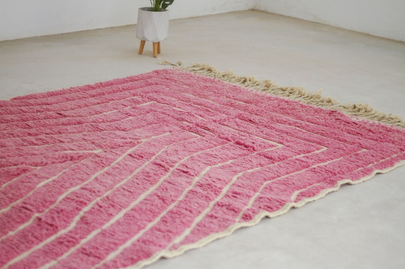 May include: A pink and white striped rug with a fringe border. The rug is made of a soft, fluffy material.