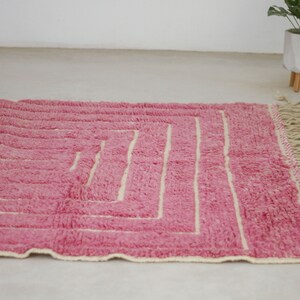 May include: A pink and cream woven rug with a geometric pattern and fringe.