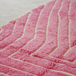 May include: Pink and white chevron patterned rug with a fluffy texture.