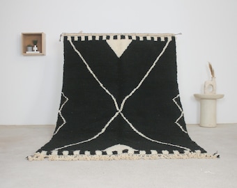 May include: A black and white geometric patterned rug with a thick pile. The rug features a central diamond design with white lines and a white triangle at the top. The edges have a fringe.