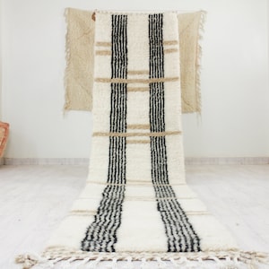 Puede incluir: Una alfombra blanca y negra a rayas con un borde beige. La alfombra está hecha de lana y tiene una textura tejida a mano.