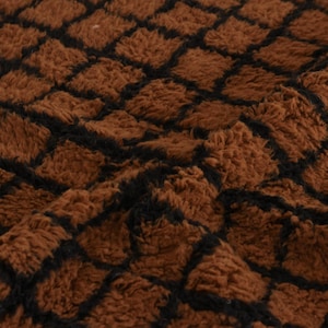 May include: Close-up of a brown, textured fabric with a repeating black grid pattern. The fabric has a soft, plush appearance, with a slightly uneven surface. The overall effect is warm and inviting.